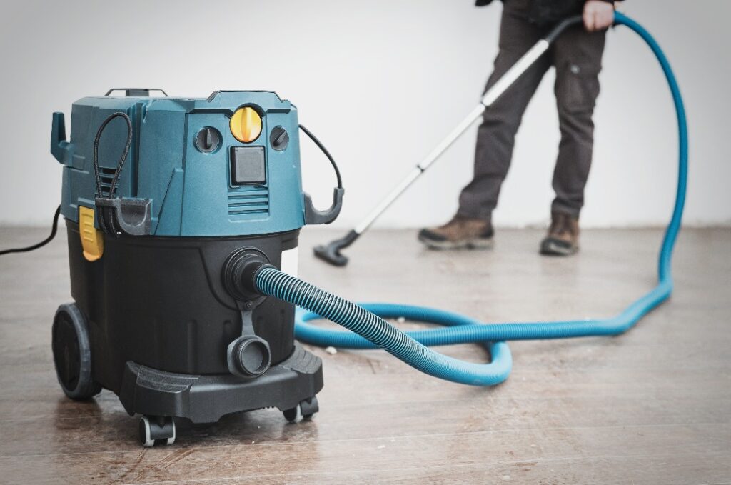 Ein Arbeiter reinigt Bauschutt nach Reparaturen mit einem großen Vakuumreiniger